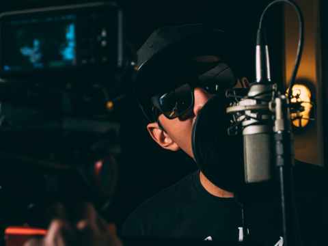 man in black cap and black framed sunglasses in front recording microphone