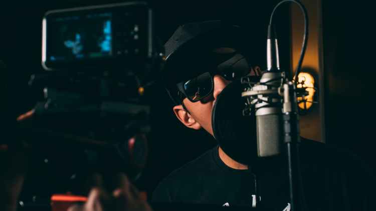 man in black cap and black framed sunglasses in front recording microphone