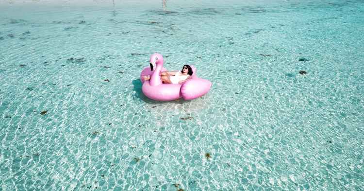 woman lying on pink flamingo bouy on body of water